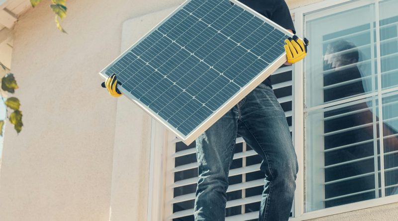 A Man in Black Shirt Standing on the Roof while Holding a Solar Panel