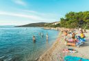 Picturesque beach scene in Skradin, Croatia with sunbathers and swimmers enjoying a sunny summer day.