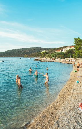 Picturesque beach scene in Skradin, Croatia with sunbathers and swimmers enjoying a sunny summer day.