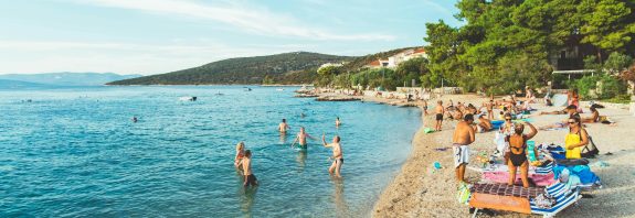 Picturesque beach scene in Skradin, Croatia with sunbathers and swimmers enjoying a sunny summer day.