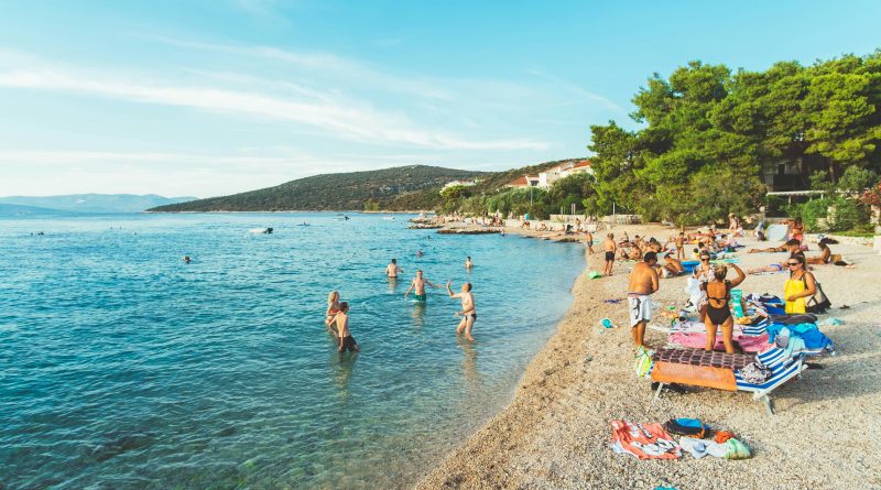 Picturesque beach scene in Skradin, Croatia with sunbathers and swimmers enjoying a sunny summer day.