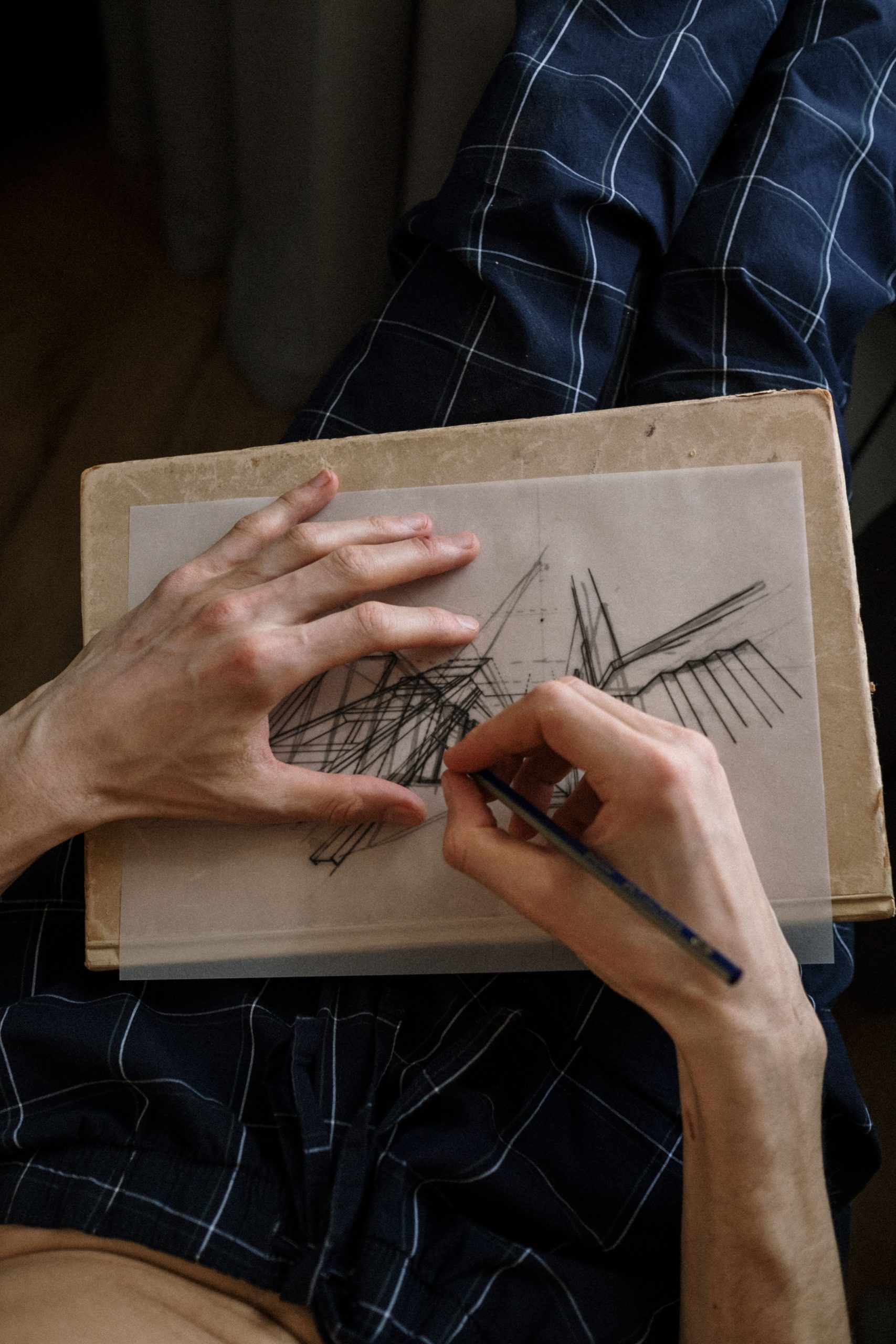Close-up of hands sketching abstract lines on paper with pencil indoors.