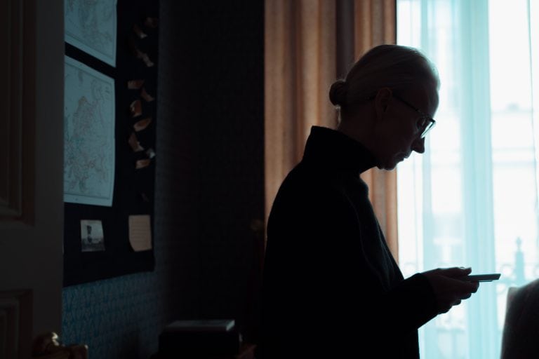 Silhouette of a senior woman looking at a smartphone in a dimly lit room, conveying introspection and solitude.